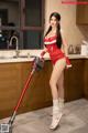 A woman in a red dress vacuuming a kitchen floor.