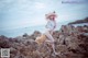 A woman in a white bikini and a straw hat on a rocky beach.