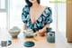 A woman sitting at a table with a teapot and cups.