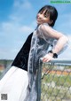 A woman in a black and white dress leaning against a fence.