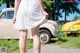 A woman in a white dress standing in front of a yellow car.