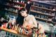 A woman in lingerie sitting at a bar with bottles of alcohol.