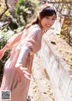 A woman in a pink dress leaning against a wall.